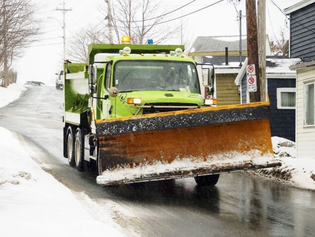 A green snow plow driving down a residential street in Syracuse