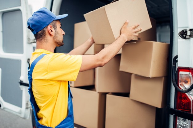 cargo-delivery-service-male-courier-uniform-with-box-hand-unloads-truck-with-cardboard-parcels-empty-container_266732-11869